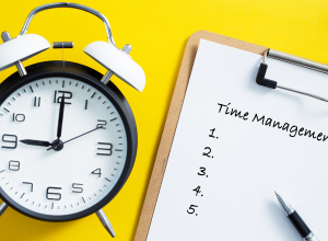 An alarm clock next to a clipboard with paper that says time management on it