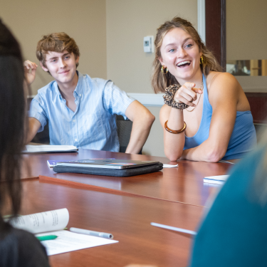 group of students sitting at a table with books and girl laughing